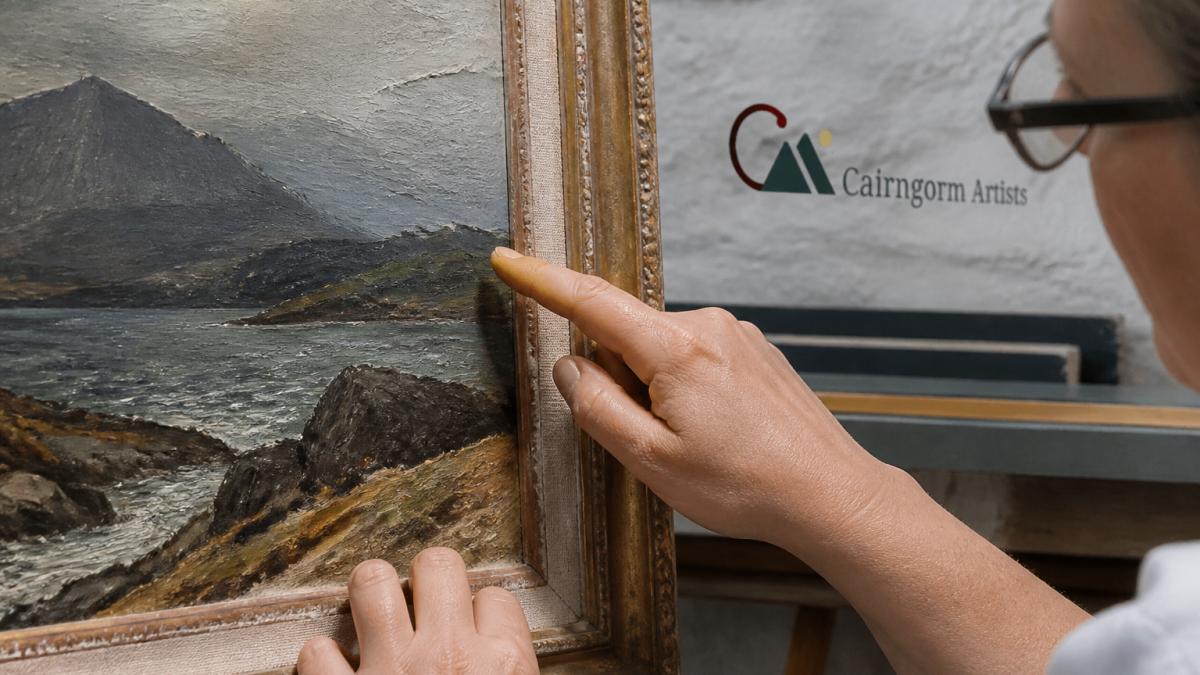 Close-up of hands examining a framed oil painting, showing detail inspection of brushwork, texture, and canvas edges under natural light