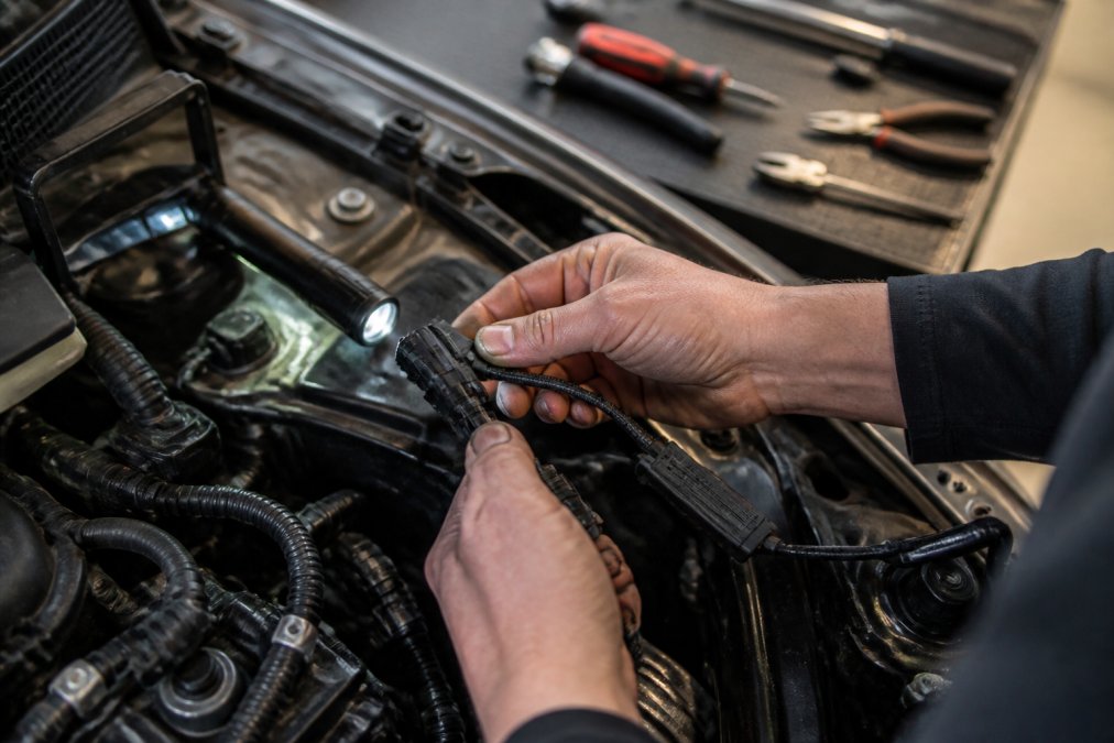 Hands connecting a plug and play LED headlight harness, a reliable iilumo alternative, inside a car engine bay.