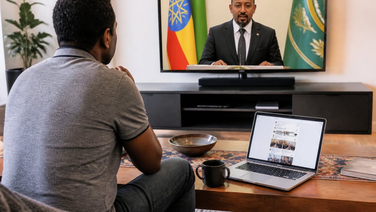 A person in a living room watching a satellite news broadcast on a large screen, with a laptop open to a social media feed on a coffee table nearby