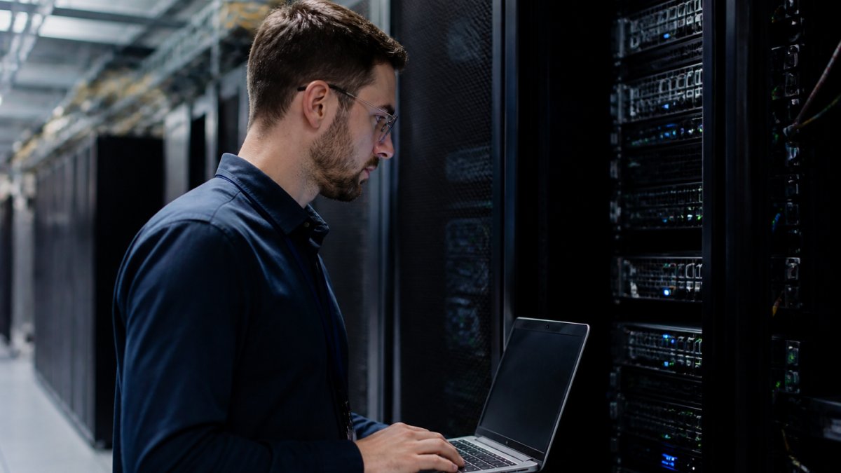 Security engineer at workstation monitoring real-time API request logs and verification dashboards on multiple monitors in secure operations center with blue screen glow and data visualizations