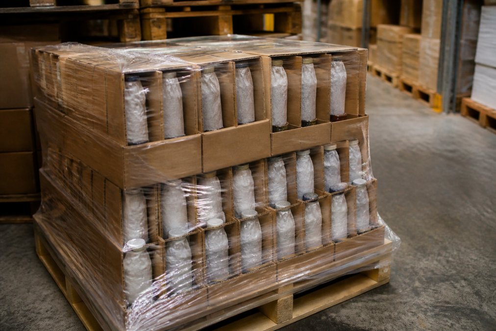 Wine bottles packed in protective wrapping and cardboard inserts, stacked on wooden pallet with shrink wrap, ready for international freight shipment in warehouse setting