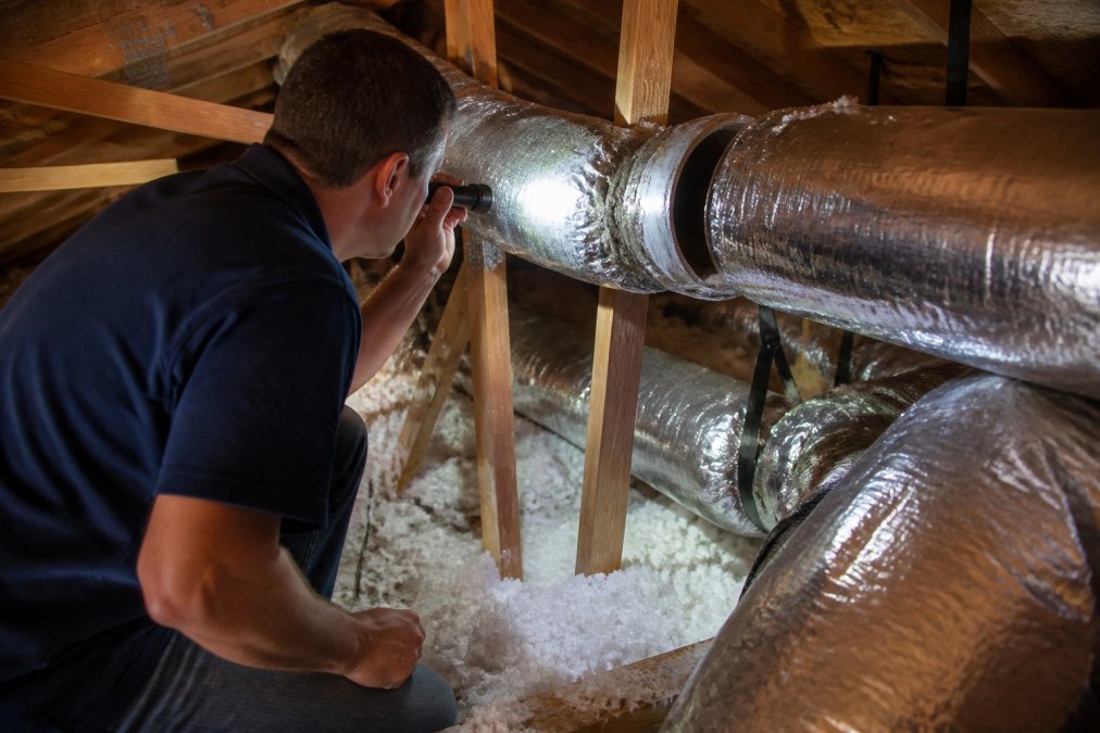 Homeowner using a flashlight to inspect attic ductwork for leaks to improve two-story airflow