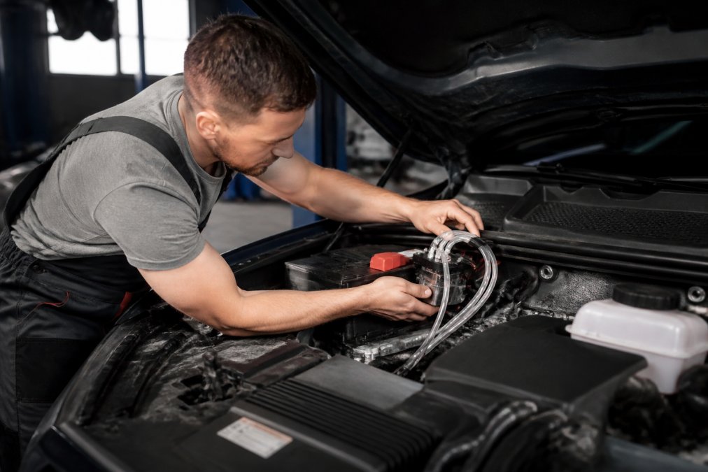 A mechanic's hands installing a compact HHO generator under the hood of a modern pickup truck, clear tubing and electrical connections visible, shop lighting overhead