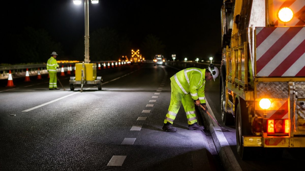 Improve Worker Safety During Night Road Maintenance Workers in high-visibility gear during night road maintenance, illuminated by beacons and portable work lights.
