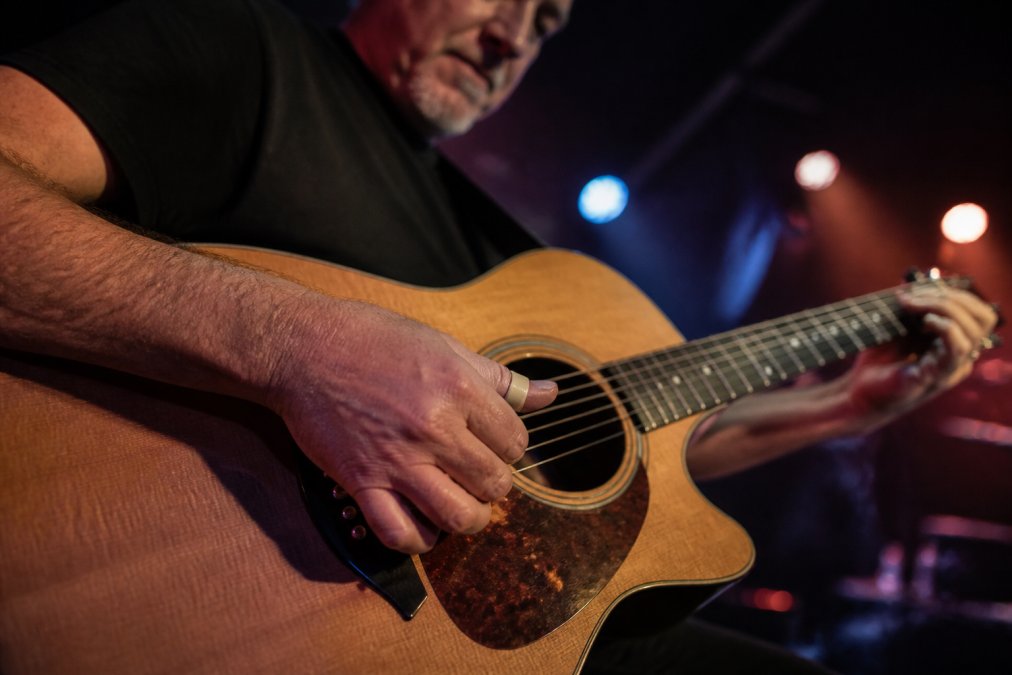 Guitarist using an ergonomic thumb pick for fingerstyle technique on acoustic guitar strings during a live show