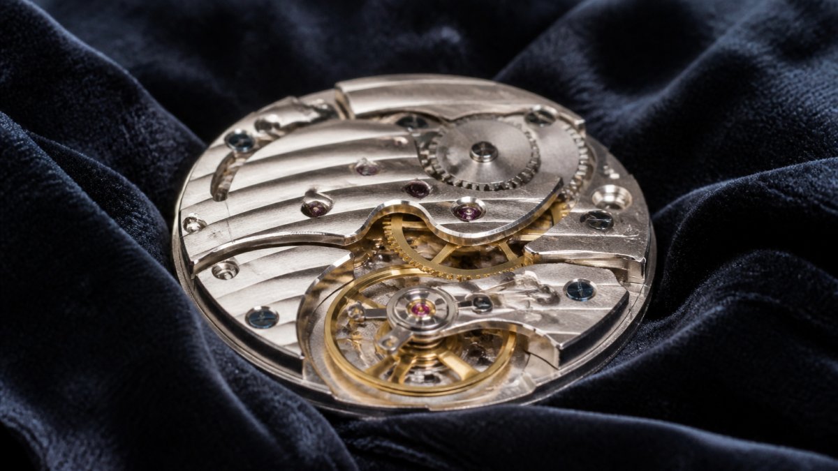 Macro photograph of an ornate hand-finished watch movement showing visible gears, balance wheel, and Geneva stripes resting on dark velvet under soft directional light