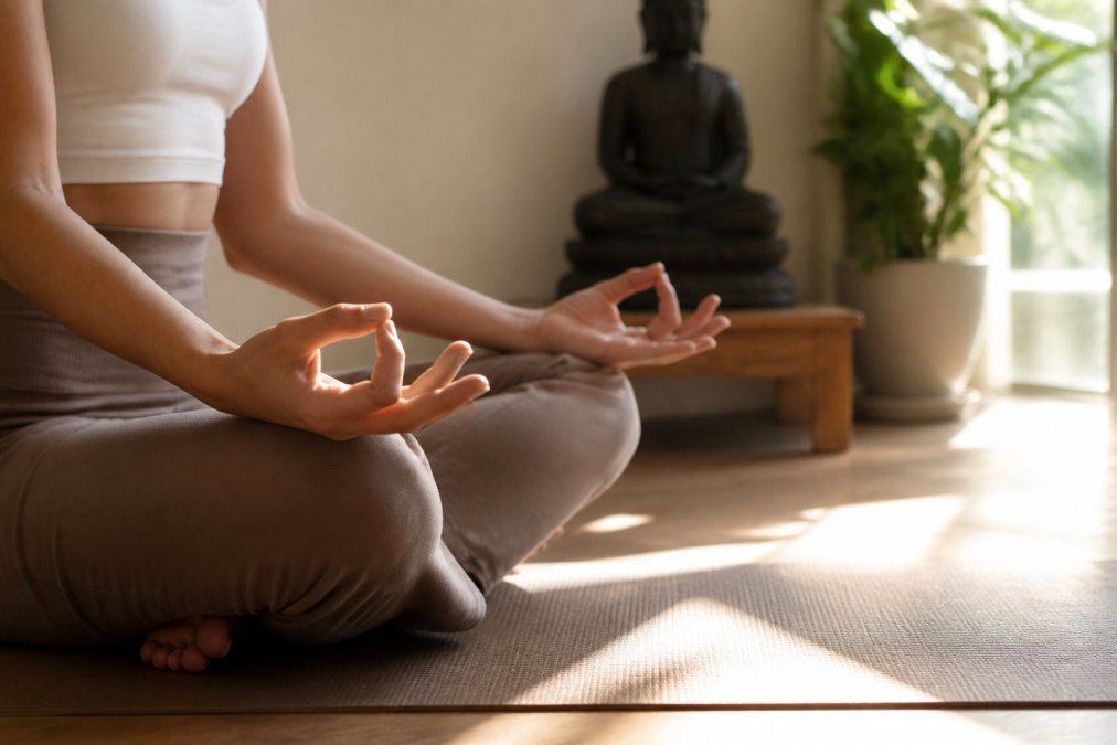 Primer plano de las manos de un practicante en Gyan mudra descansando sobre las rodillas en una pose de meditación sentada con las piernas cruzadas, luz natural suave en un tranquilo estudio casero