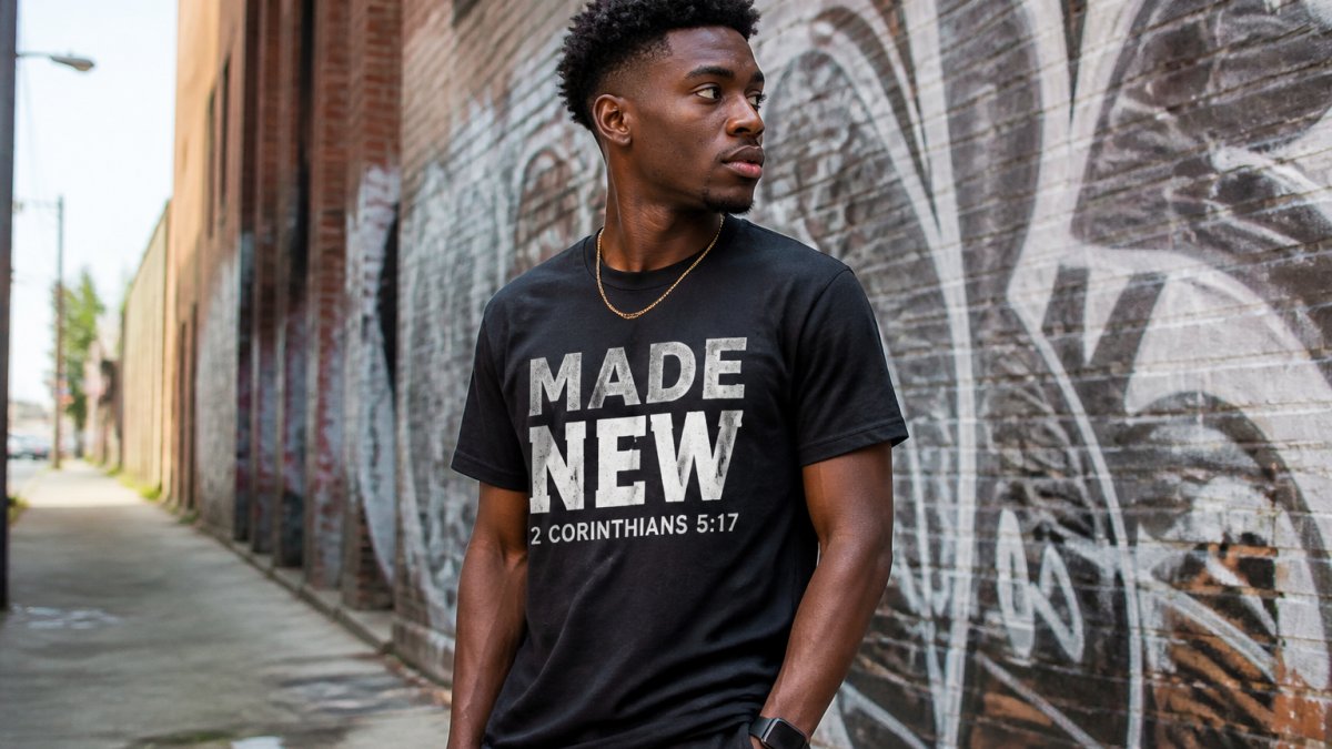Young adult wearing bold faith-inspired streetwear tee with visible scripture graphic in urban setting with confident posture and natural street lighting