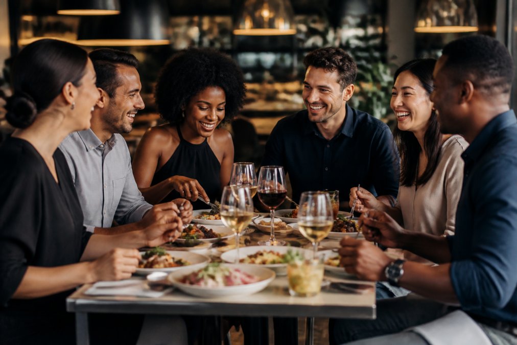 A diverse group of diners enjoying a meal together at a local restaurant, smiling and engaged in conversation over appetizers and drinks in warm lighting