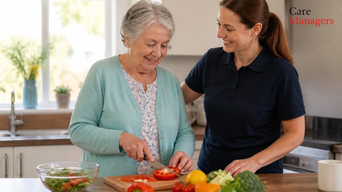 An older adult smiling while preparing a meal in a bright, modern kitchen, with a care worker standing nearby offering gentle assistance, warm natural light through the window