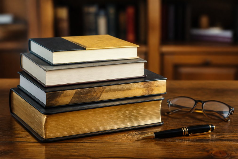 Stack of gold investment books and guides displayed on a wooden desk with reading glasses and a pen nearby