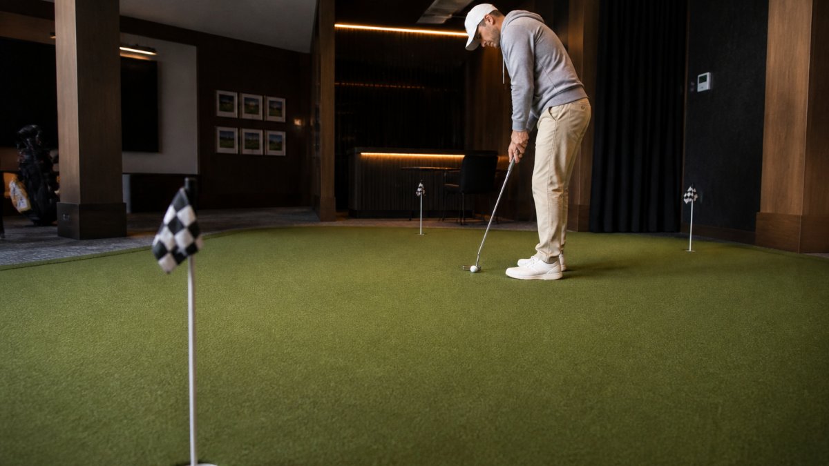 A golfer lining up a putt on an indoor putting green with projected alignment lines glowing on the surface, dimly lit premium studio setting