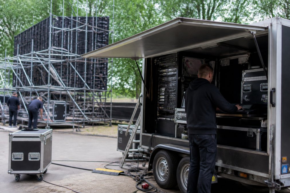 Een mobiele LED-aanhangwagen met regieruimte opgesteld op een evenemententerrein, met technicus die de installatie voorbereidt