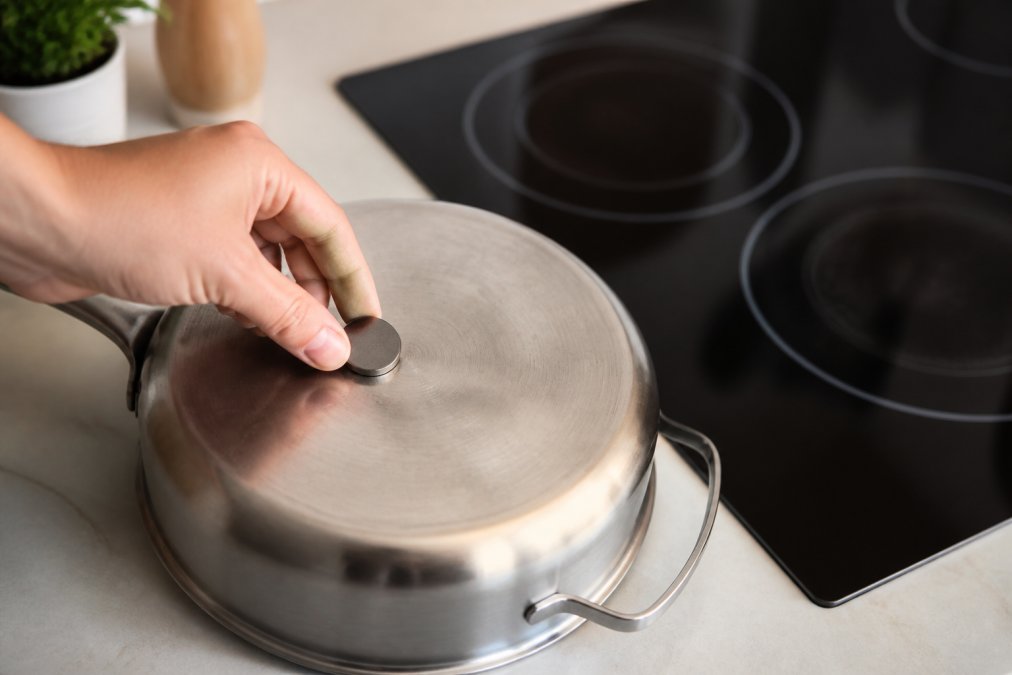 Person testing the base of a stainless steel pan with a magnet near an induction cooktop
