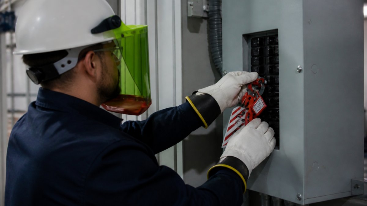 Technician in PPE applying lockout tagout devices to an electrical panel for industrial electrical safety compliance in