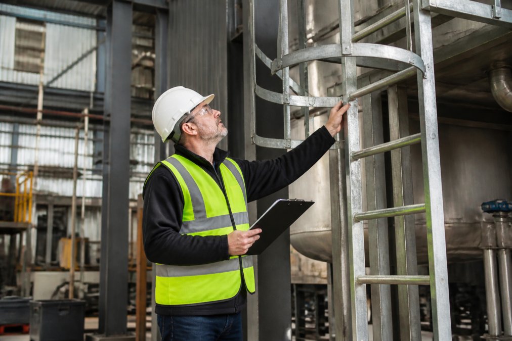 Safety inspector checking industrial ladder safety standards on a fixed ladder in a manufacturing plant