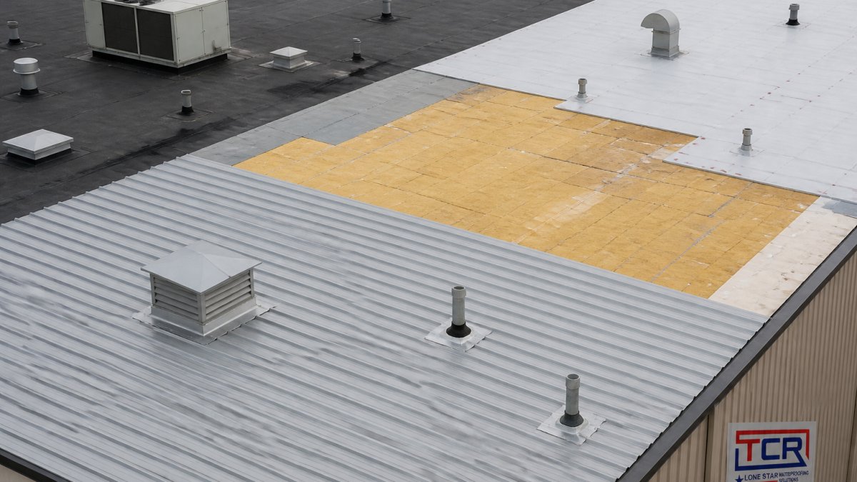 Overhead view of industrial facility roof showing different roofing material sections, metal panels, insulation, and roof penetrations with HVAC equipment and flashing details visible