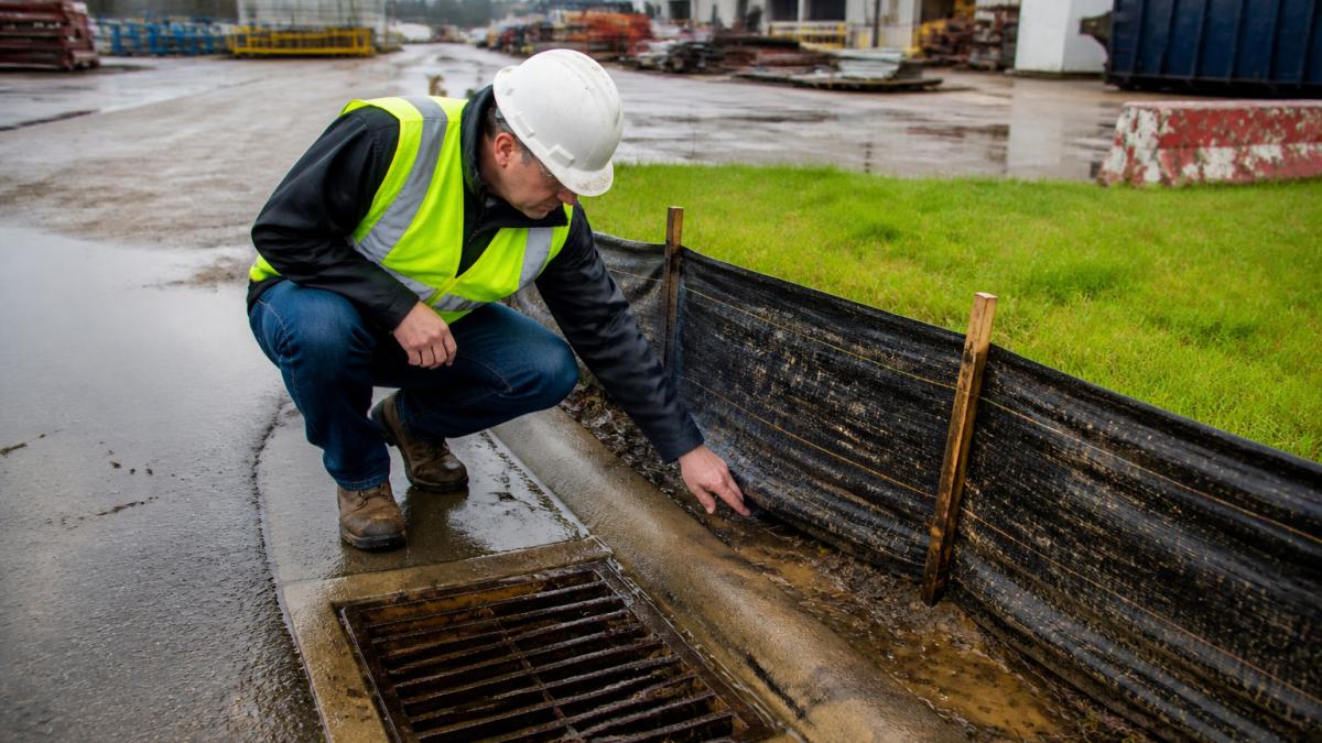 Technician inspecting a sediment barrier to prevent stormwater exceedance at an industrial drainage site