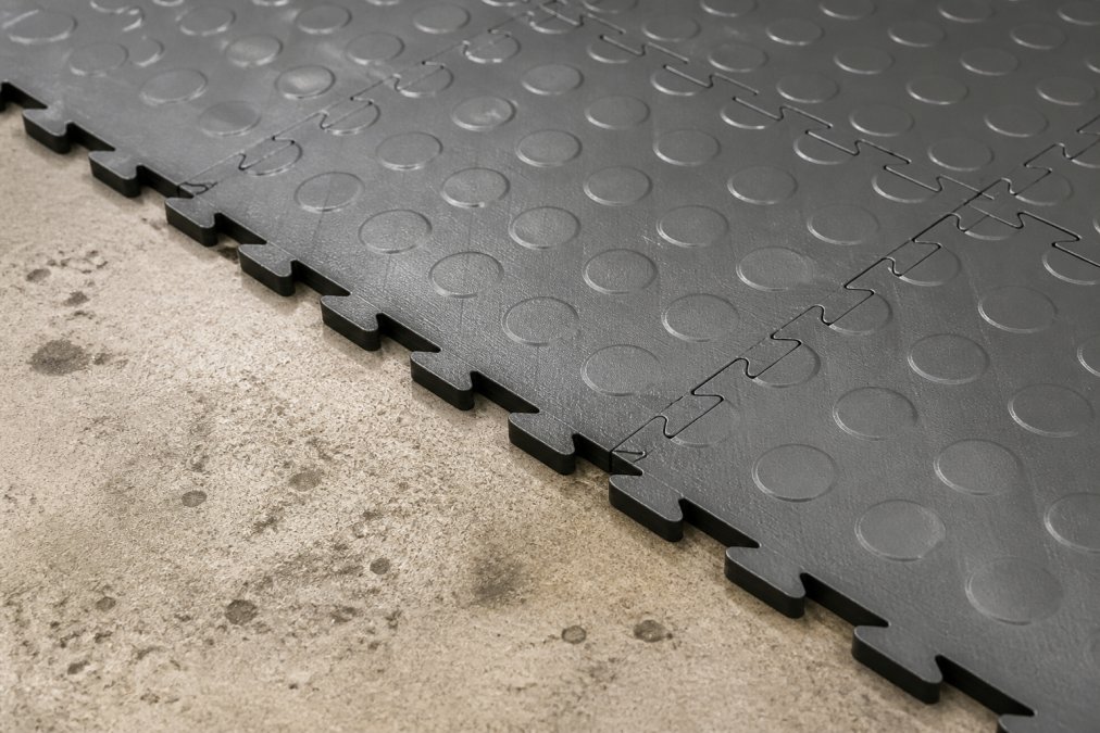 Industrigulve med høj slidstyrke: Pris og valg 2 Close-up of interlocking PVC industrial floor tiles showing texture, durability, and modular design, arranged on concrete surface with professional lighting