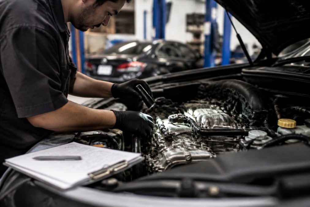 Experienced technician's hands performing detailed diagnostic inspection of luxury vehicle's internal engine components with precision instruments and technical documentation visible