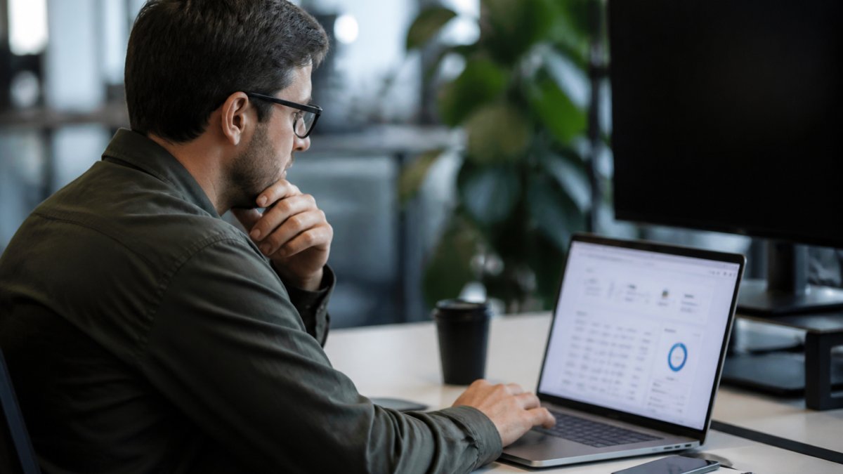 Professional marketing manager reviewing campaign analytics dashboard on laptop screen in modern office with multiple monitors displaying real-time performance data