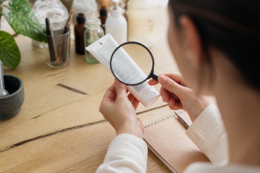 Person examining a toothpaste tube label with magnifying glass in natural lighting, ingredient list clearly visible