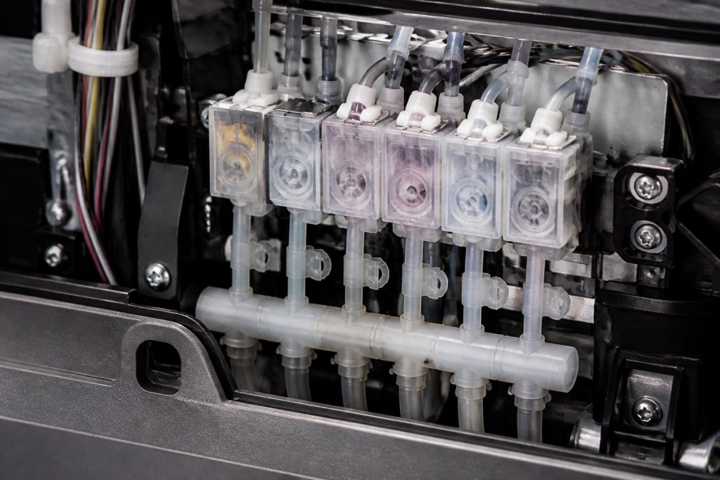 Close-up of printhead assembly showing ink delivery tubes, damper components, and internal ink circulation channels with professional workshop lighting