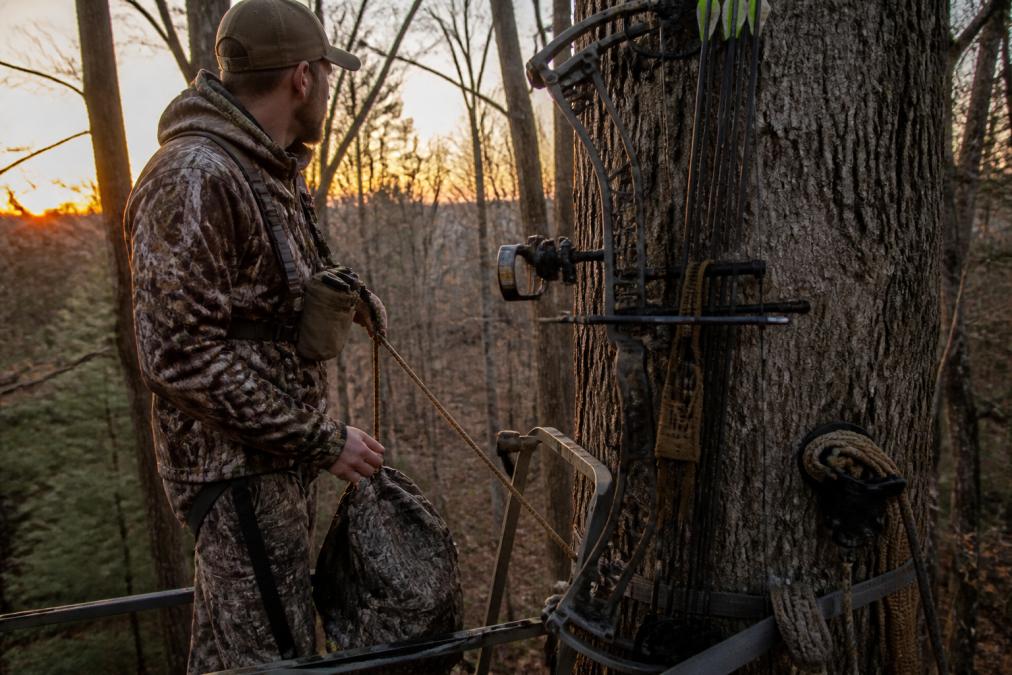 Hunter in a tree stand with a fully organized mobile bow hunting setup at dawn