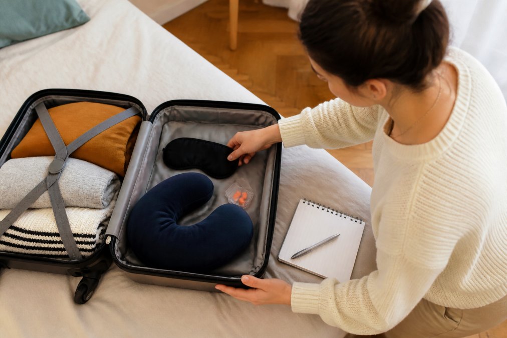 Valise ouverte avec accessoires pour éviter l'insomnie voyage : masque, bouchons d'oreilles et checklist.