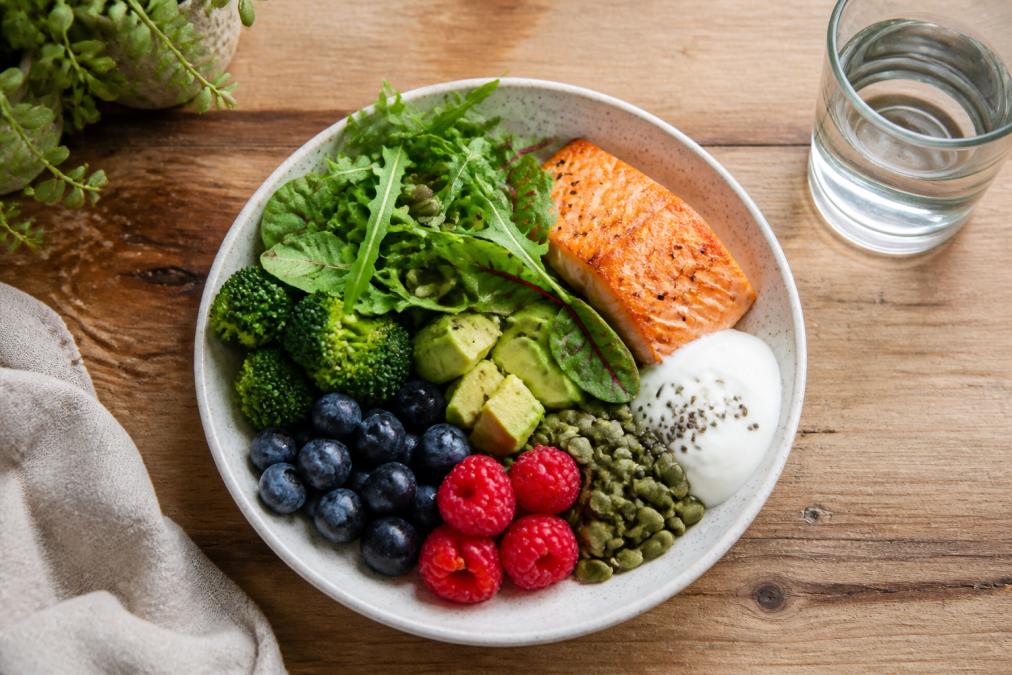 Healthy hormone-promoting whole foods on plate, avocado, berries, egg, brocolli and greens.
