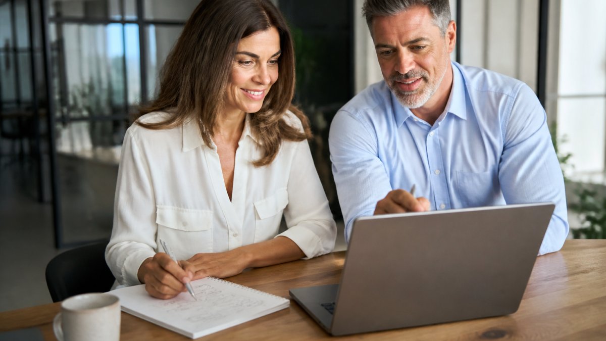 Consultant and owner reviewing an intelligent sales workflow diagram on a laptop at a bright office desk