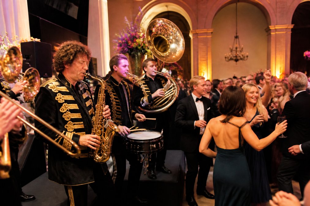 Professional brassband in traditional attire performing energetically on a decorated stage while guests dance and enjoy the festive atmosphere at an elegant gala evening