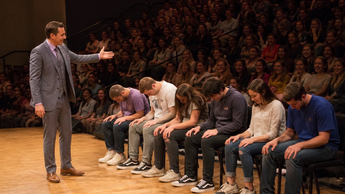 A performer gestures toward student volunteers on stage during one of our interactive stage shows for college audiences.
