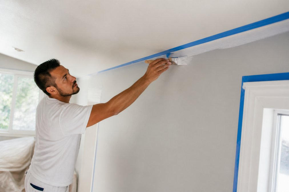 Professional painter using an angled brush to cut in paint along a ceiling line during an interior painting project