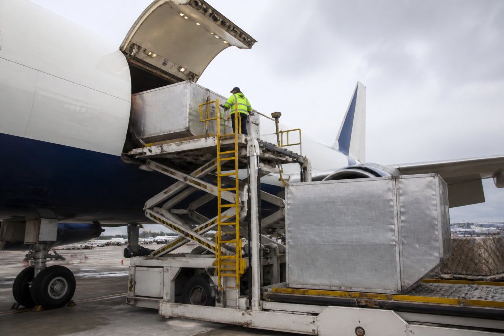 Commercial cargo airplane on tarmac with ground crew loading large metal shipping containers, showing the scale and operational efficiency of air freight loading
