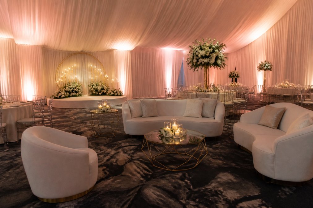 An elegant event space with luxurious white draping, a professional lounge furniture setup, and warm uplighting creating an opulent ambiance for a small wedding reception
