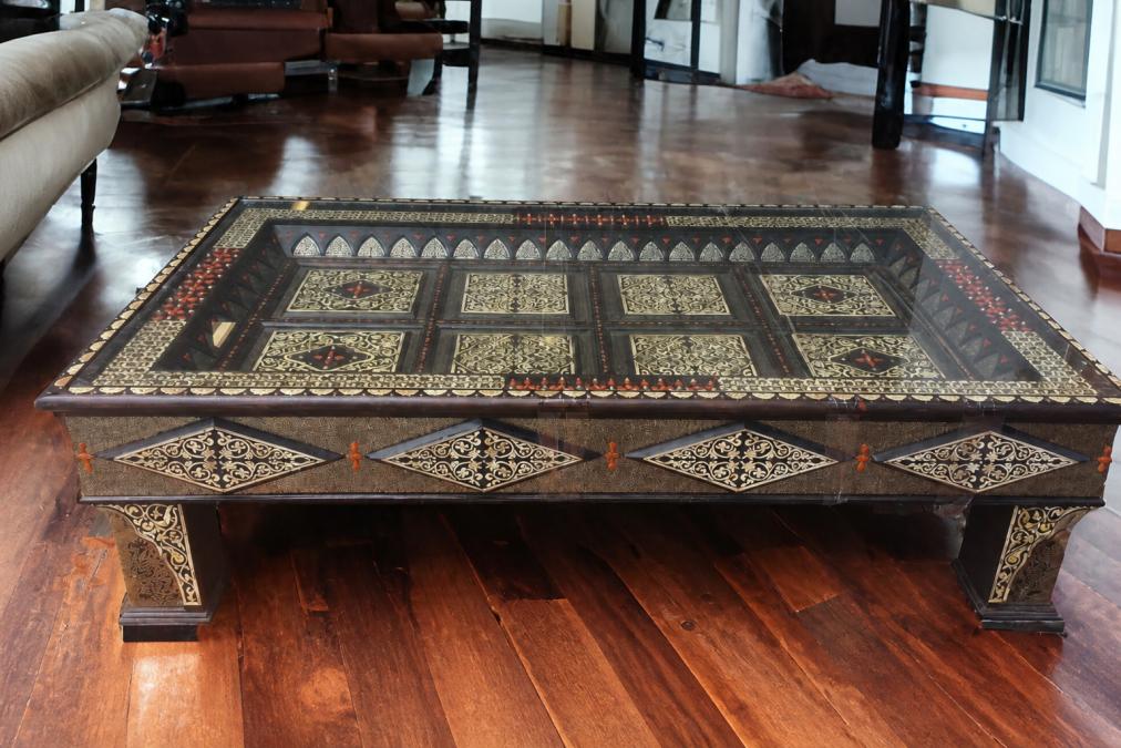 Close-up of an ornate camel bone inlaid table with intricate geometric patterns and silver metal accents, showing detailed hand-carved details under warm gallery lighting