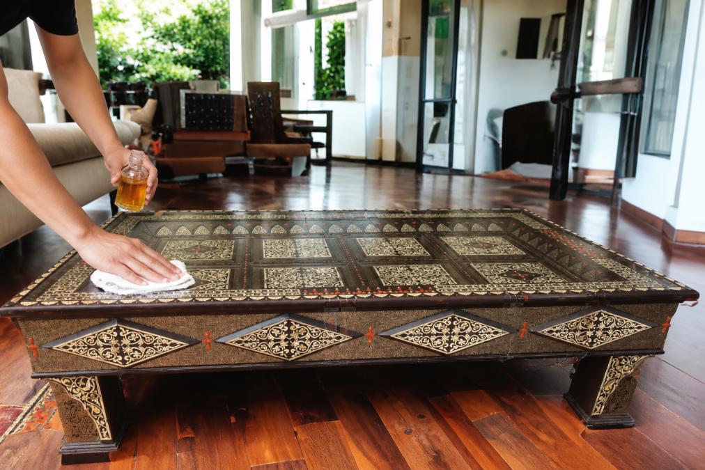 Hands carefully cleaning and polishing a decorative wooden Moroccan piece with visible natural wood grain, demonstrating proper maintenance technique with soft cloth and natural oil