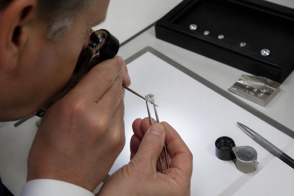 Professional gemologist examining a certified diamond under bright magnification lighting with a loupe, revealing the stone's internal clarity and sparkle against a white examination surface
