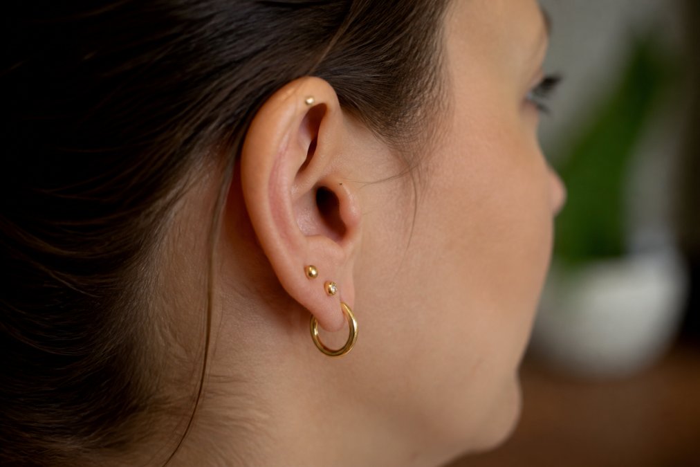 Woman with multiple healed ear piercings wearing small solid gold hoop and stud earrings in soft lighting