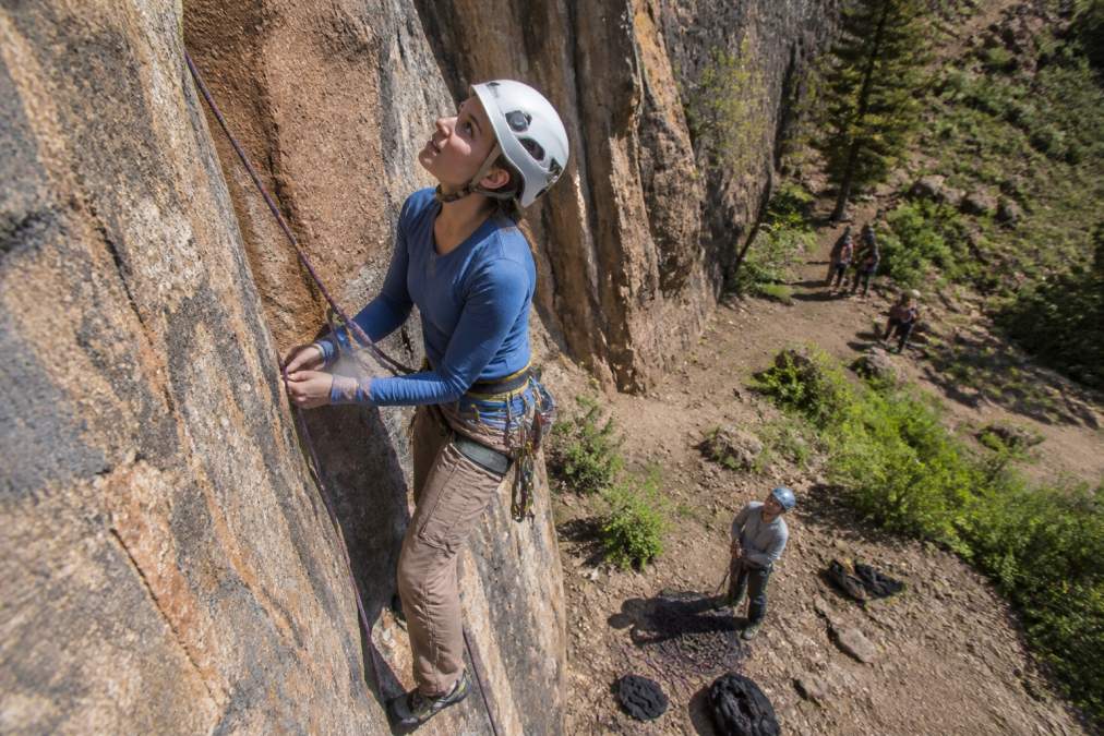 Climber wearing a protective helmet and harness on a sunny multi-pitch rock wall with a belayer below