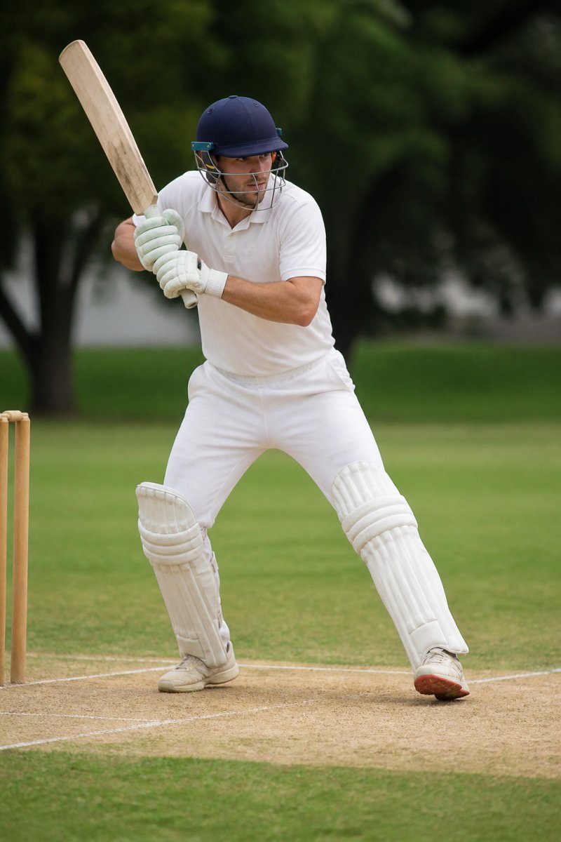 Professional cricketer demonstrating proper batting stance and weight distribution during a shot, showing hand position and grip on the bat at the crease