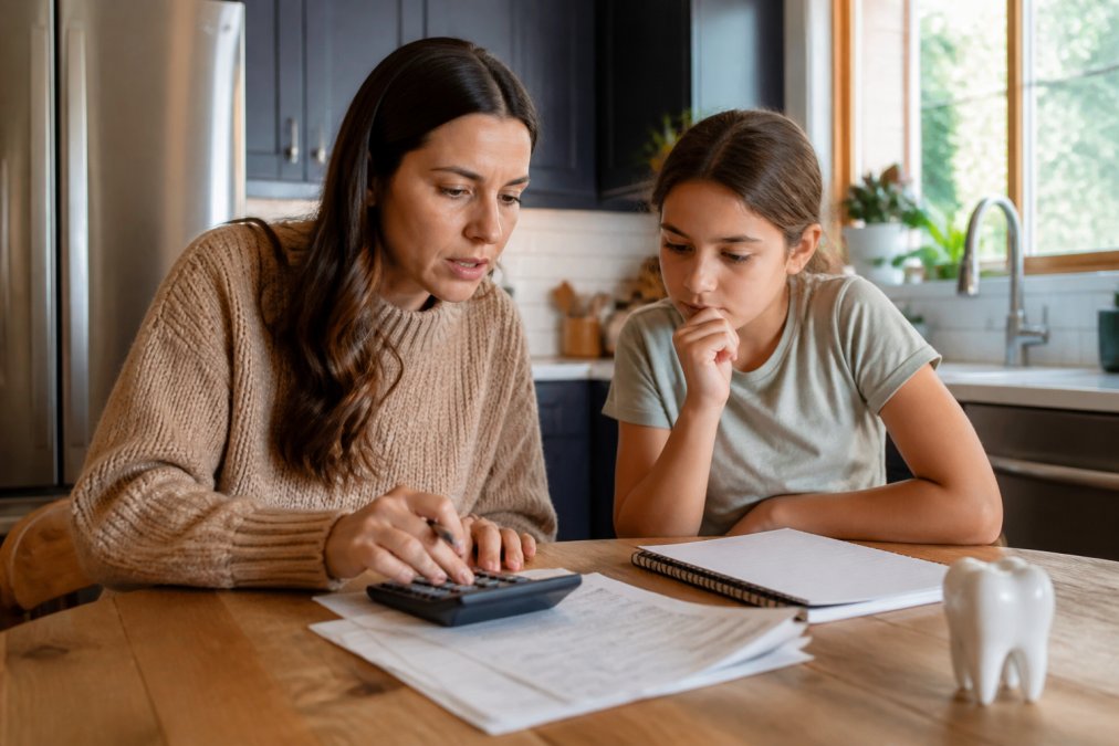 Parent and child using a calculator to compare expenses for a dental savings plan at a kitchen table