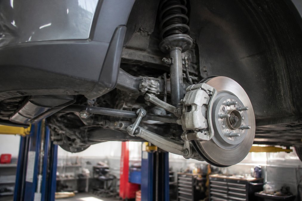 Close-up view of electric vehicle suspension components, control arms, and brake assembly in a service bay with diagnostic equipment visible