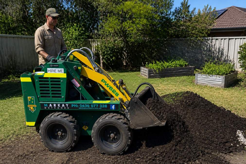 Homeowner using a kanga loader residential machine to shift topsoil in a suburban garden renovation project.