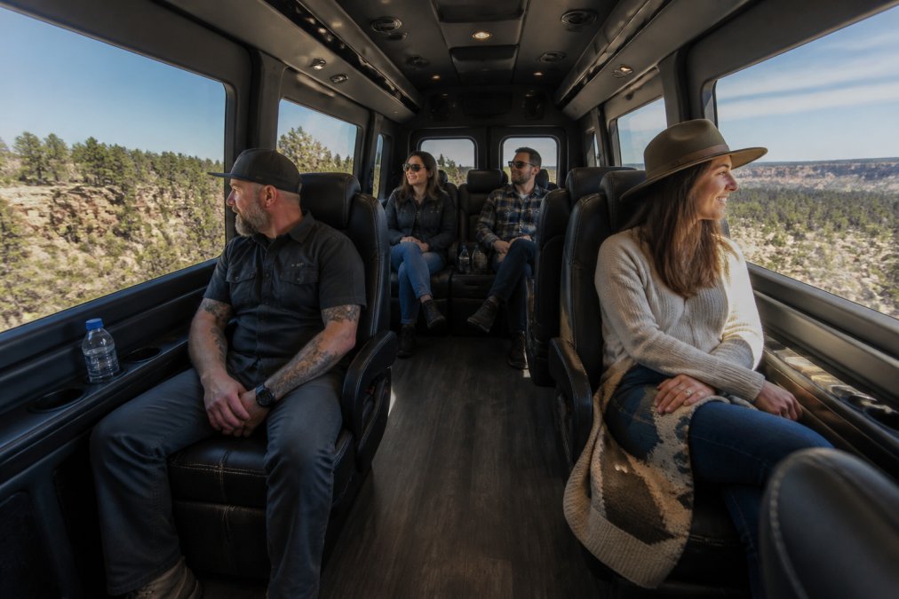 Interior view of an upgraded Ford Transit van with flexible seating, showing spacious legroom and upscale furnishings, with passengers relaxed and enjoying the ride through scenic landscape