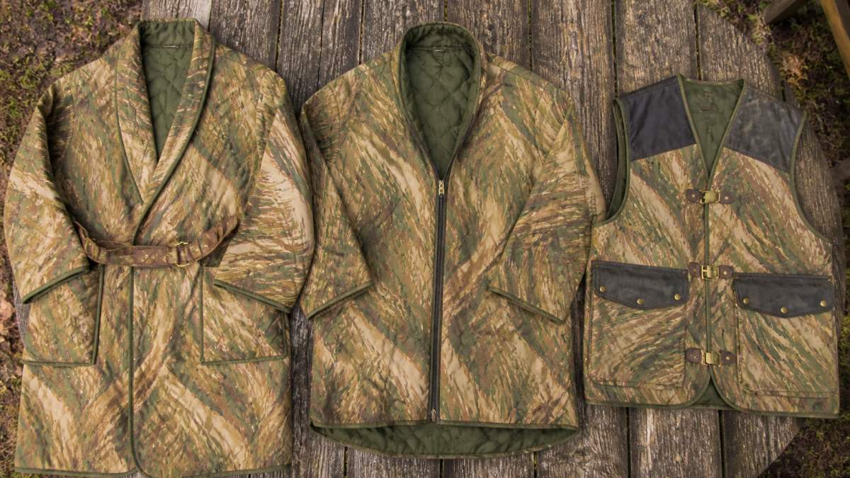 Three camouflage garments in Rhodesian brushstroke pattern laid flat on weathered wood planks outdoors