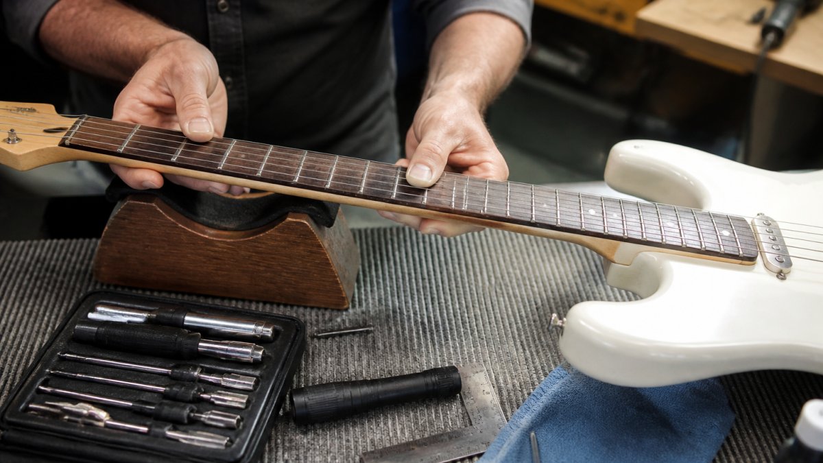 Hands inspecting the neck and fretboard of an electric guitar for signs of wear in natural light