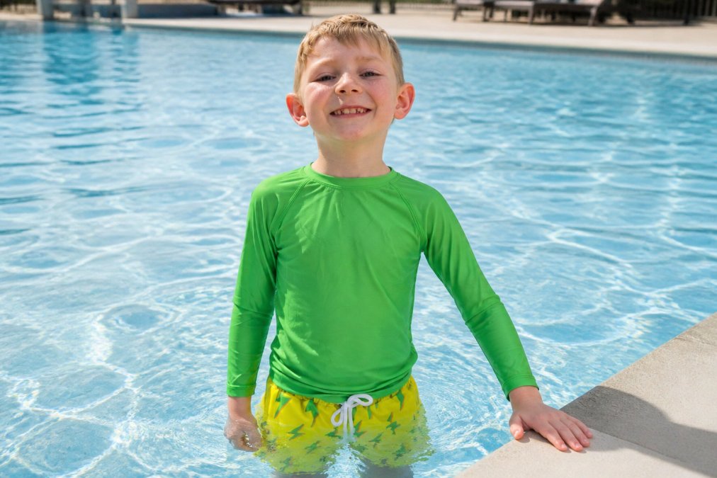 Young child wearing bright neon high-visibility swimsuit in the water, standing out clearly against the blue pool environment, with excellent visibility and contrast