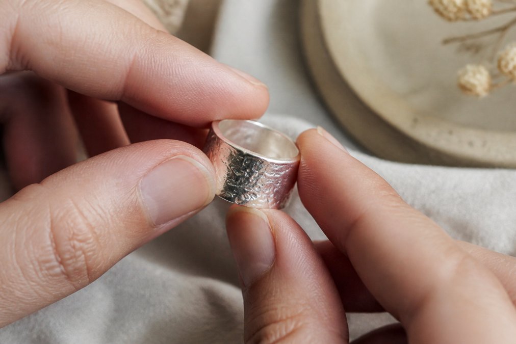 Close-up of hands examining a sterling silver ring under natural light, showing the craftsmanship details, finish quality, and surface texture of the band